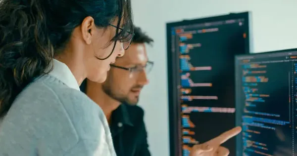 Grupo de personas colaborando mientras revisan código HTML en pantalla grande, reflejando el desarrollo técnico en diseño de páginas web.