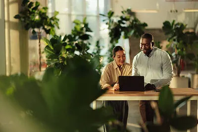 Por qué mi negocio nuevo no vende con dos personas reunidas en una mesa de trabajo, utilizando una computadora portátil, revisando documentos impresos y conversando sobre estrategias para impulsar su negocio.